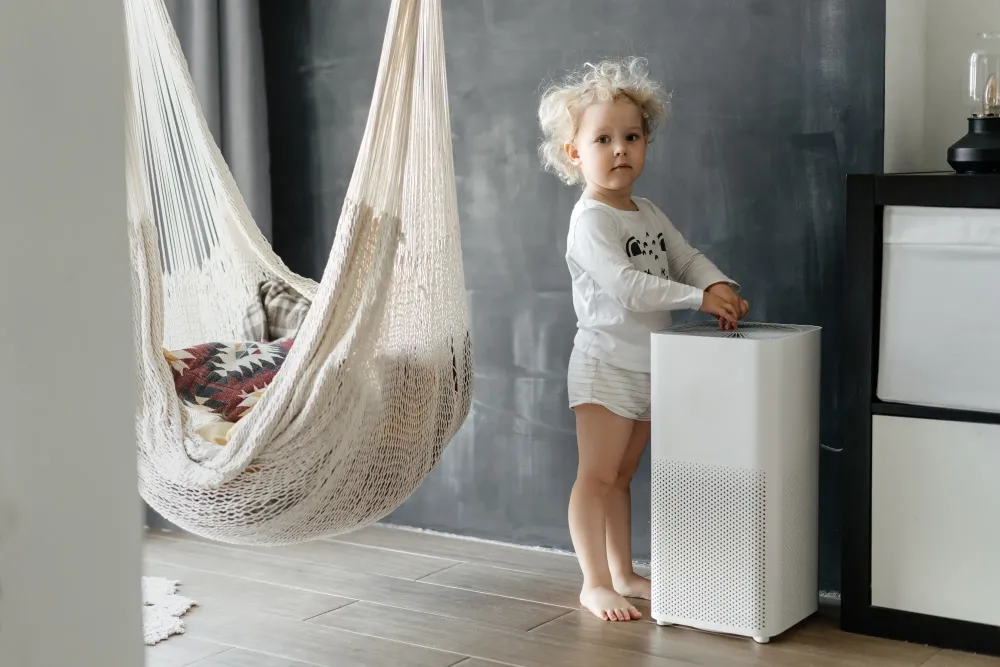 A small child sitting next to an air purifier, happily breathing in fresh and clean air at home