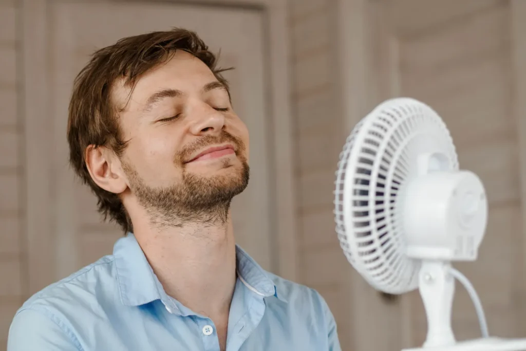 Sweaty man feeling refreshed by the cool air from a fan